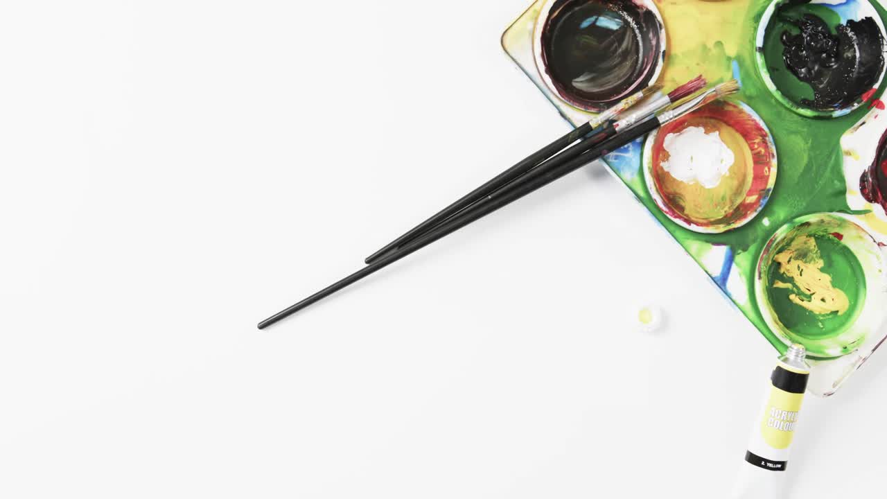 vista aérea de pinturas y pinceles sobre fondo blanco, en cámara lenta