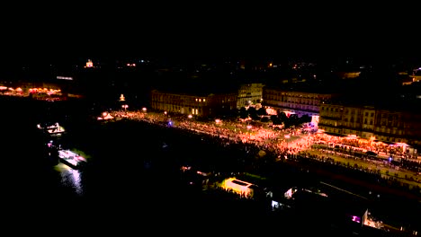 people gathering in quai du maréchal square during wine fair at night in bordeaux france, aerial pan right shot