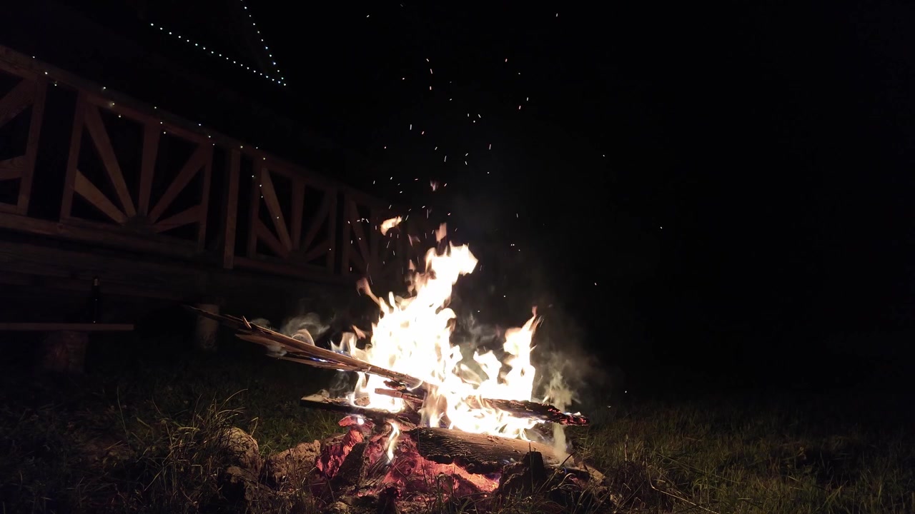 Fogueira atmosférica iluminando a grama verde em uma noite tranquila. Chamas brilhantes e faíscas flutuantes criam uma cena mágica ao ar livre para acampamento e projetos de natureza
