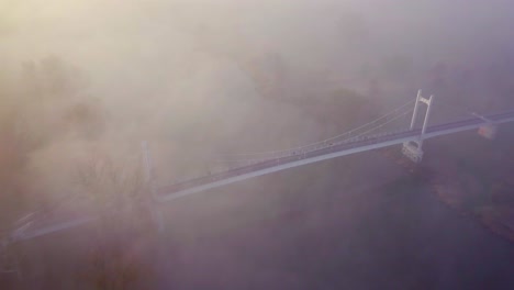 Aerial-shot-of-a-pedestrian-suspension-bridge,-shot-during-sunrise-and-heavy-fog-in-Wroclaw,-Poland