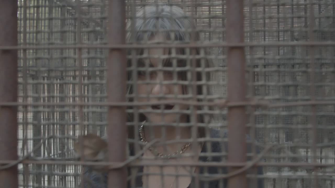 경멸적인 표정으로 철장 안에 서 있는 표현 화장을 한 검은 드레스를 입은 소녀