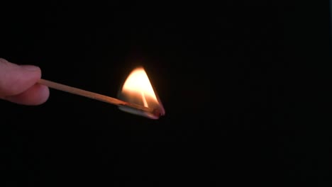 hand holding a burning match facing down with a black background