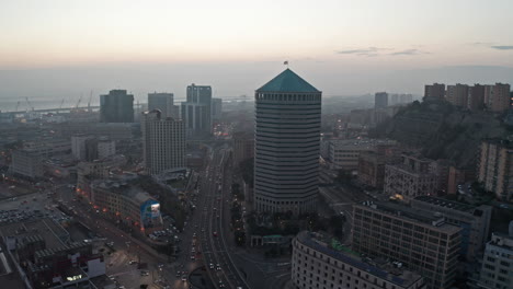 aerial view of a bustling city at dusk with a prominent skyscraper and harbor