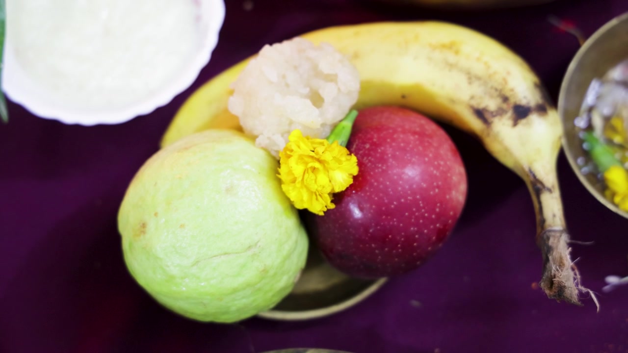 Offerte tradizionali puja indù con banana, mela, guava e dolci sacri durante una cerimonia religiosa.