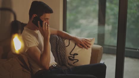 Young-Man-Talking-On-The-Phone-While-Sitting-On-The-Couch-In-The-House