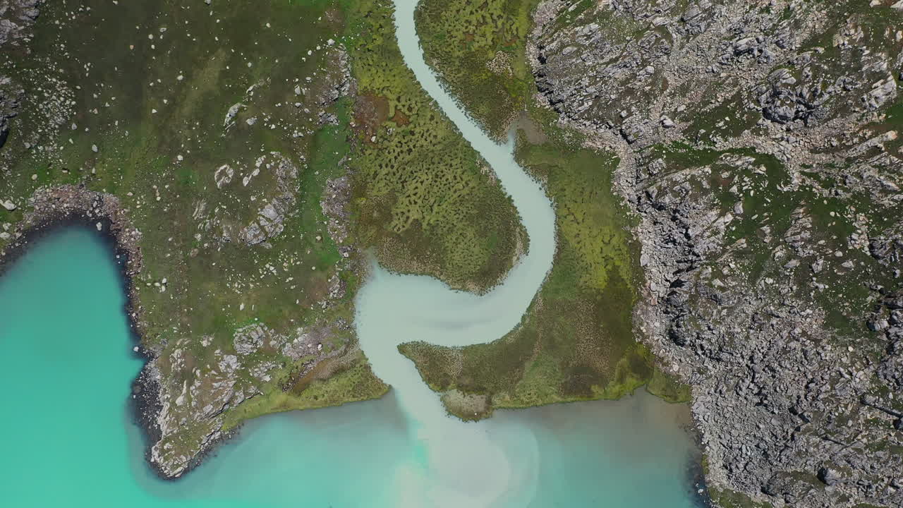 Záběr z dronu odhalující řeku ústící do jezera Ala-Kol v Kyrgyzstánu, snímaný shora.