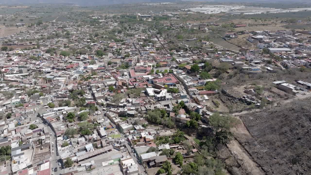 Amatitan municipality neighbourhood in Mexican state of Jalisco surrounded by blue agave agricultural fields, Catholic church Parish of the Immaculate Conception in view, establishing drone shot