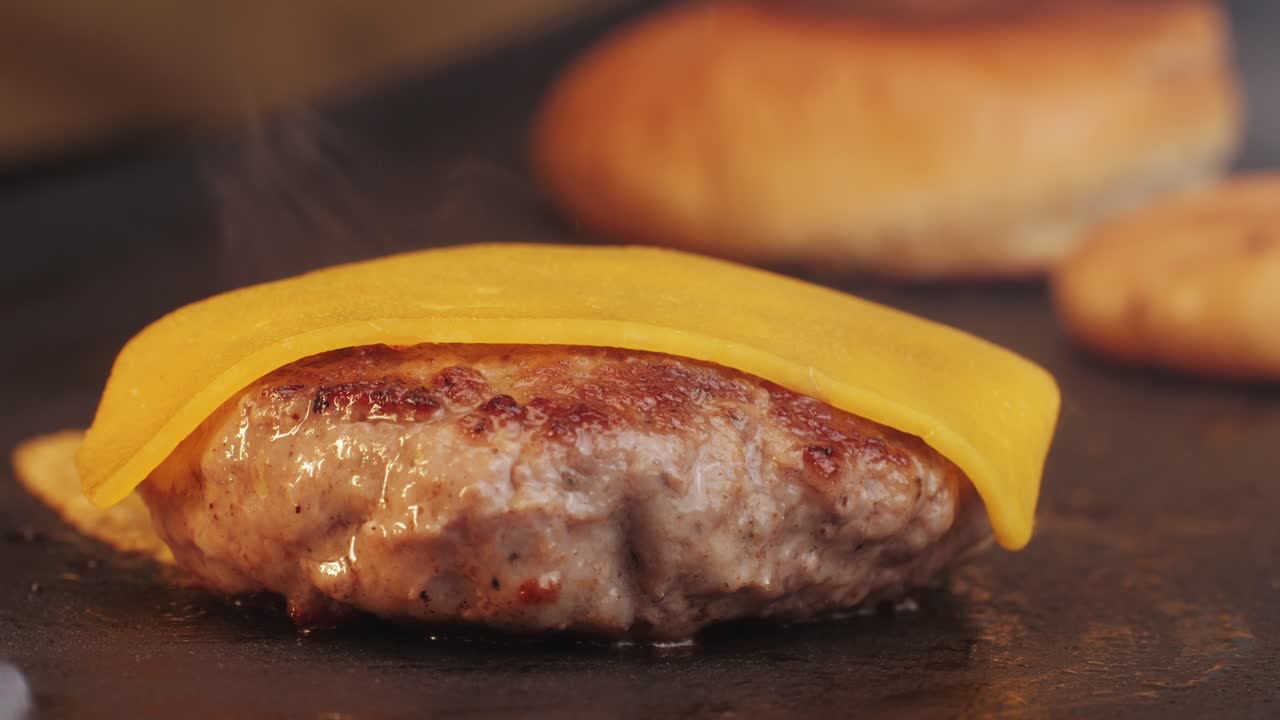 Cooking American fat smash burger with cheese slice on top on grill close-up. Beef or pork cutlet smashing by burger press. The chef in kitchen of the restaurant making cutlets for burgers - smash burger beefsteak. Fast and street food concept.