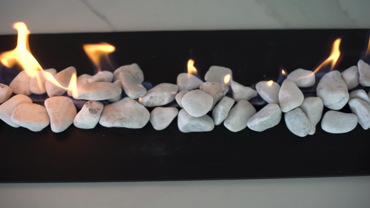 흰색 자갈이 있는 실내 가스 화재 장소 위에서 슬로우 모션 추적 샷을 닫습니다.