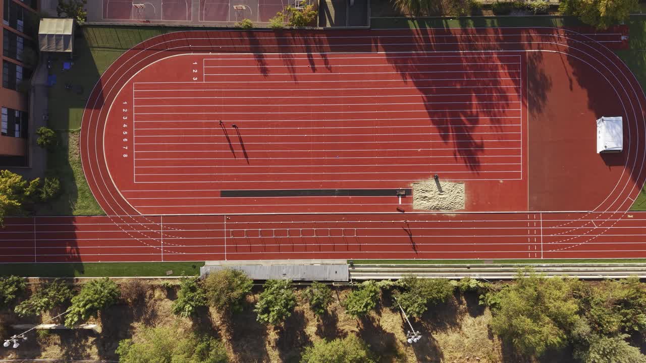 Droneoptagelse ovenfra af en person, der løber på en rød atletikbane ved Colegio Cumbres på en klar, solrig dag. Chile, 4K.