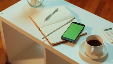 [camera used: arri alexa, 50mm lens, slow motion] slow pan of a green screen cell phone with tracking marks, placed on a coffee table at a coffee shop or living room setting