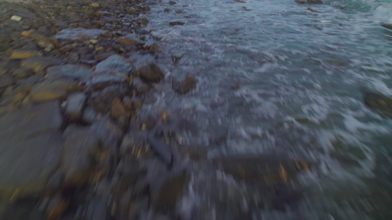 Drone flying low over a rocky coastline, birdseye view tilting up into the horizon
