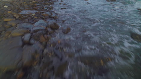 Drone-flying-low-over-a-rocky-coastline,-birdseye-view-tilting-up-into-the-horizon