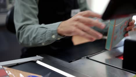 unrecognizable sales clerk working at grocery store. male cashier in black apron in supermarket at cash desk