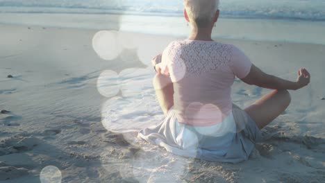 Animación-De-Puntos-De-Luz-Sobre-Una-Mujer-Caucásica-Mayor-Practicando-Yoga-En-La-Playa-Y-Meditando