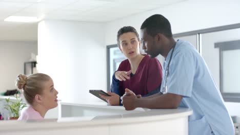 diverse doctors talking to medical receptionist sitting at front desk at hospital, slow motion