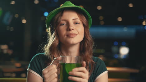 retrato de una mujer joven y bonita con una jarra de cerveza verde y con un sombrero irlandés