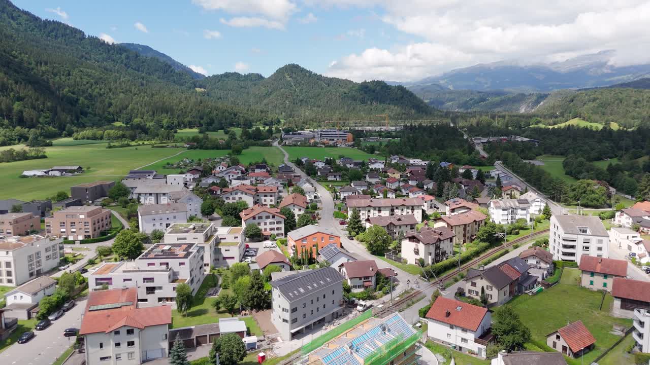 Industrial cargo train on tracks in Swiss town of Bonaduz, Switzerland. Sunny summer day in historic city. Green mountain alps in distance. Aerial wide shot