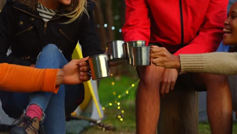 amigos brindando tazas de café cerca de una fogata en el bosque 4k