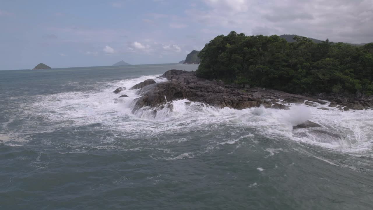 vuelo orbital sobre una isla con rocas y árboles en el océano, cielo azul detrás