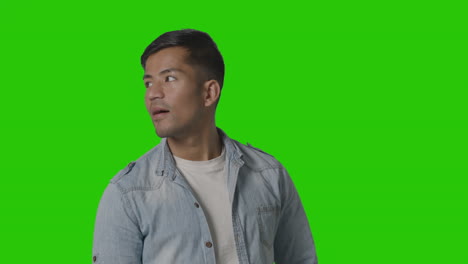 portrait of casually dressed smiling young man looking around against green screen