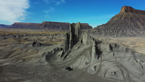 aerial view of man running uphill on a grey sandstone hill followed by black suv vehicle