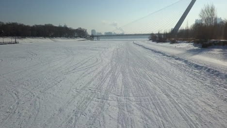 low aerial flight along tracked frozen river surface to cable bridge