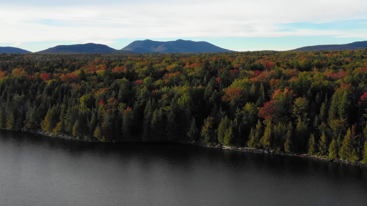 toma aérea de drones deslizándose a la izquierda a lo largo del borde de un lago con coloridos árboles de otoño a lo largo de la orilla cuando termina el verano y la temporada cambia para caer en maine