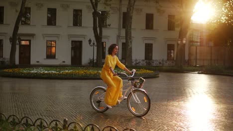 young woman riding a city bicycle with a basket and flowers in the city center during the dawn enjoying her time early in the