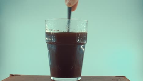 un primer plano de un vaso de café negro revolviendo con una cuchara de plata, granos de café flotantes, luz de estudio, video de 4k