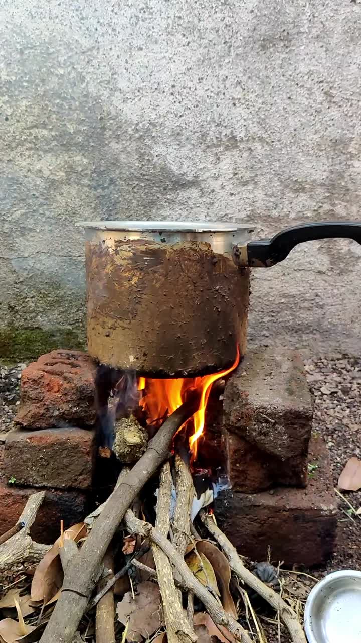 In an open space in Maharashtra, India, food is being prepared on a traditional chulha. Wood crackles under the slow-motion flames as a metal cooker sits atop, capturing rustic village cooking