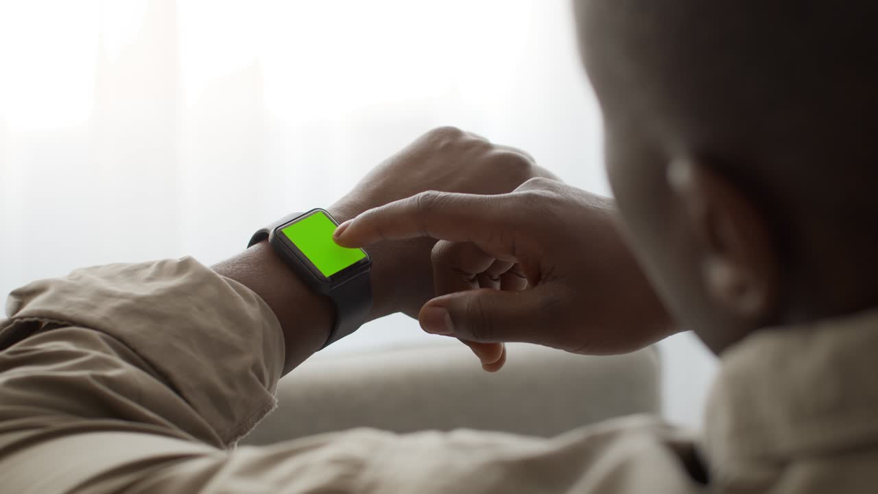African american man scrolling green chroma key screen of smartwatch, reading message or checking his health condition