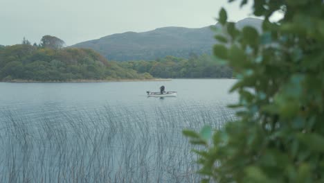 Fisherman-fishing-from-lake-boat-anchored-in-bay-beyond-reeds