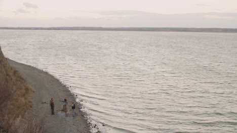 vista de drones de un grupo de amigos adolescentes alrededor de la hoguera mientras beben té y comen salchichas en la orilla del mar