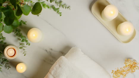 overhead view looking down on still life of lit candles with dried grasses green plant and person putting down towels as part of relaxing spa day decor