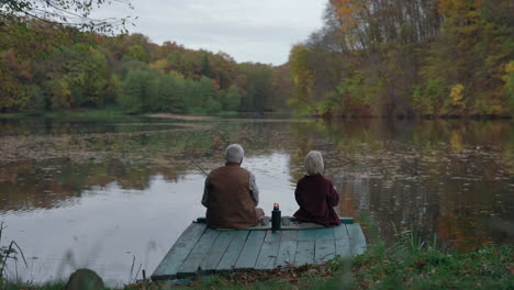 two people fishing on a dock in a scenic autumn landscape