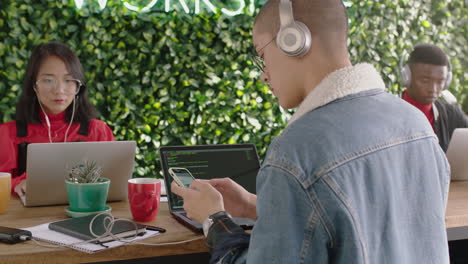 young mixed race man business student using smartphone browsing social media texting enjoying online study listening to music wearing headphones