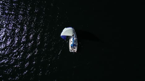 Sailboat-seen-from-above,-colorful-sail,-dark-water,-sunlight,-calm-sea