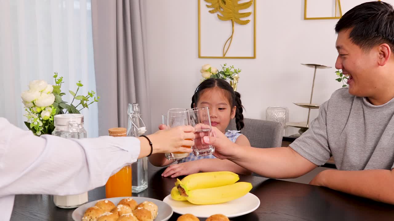 A family shares a joyful breakfast, clinking glasses of juice and milk, in a warmly lit dining room