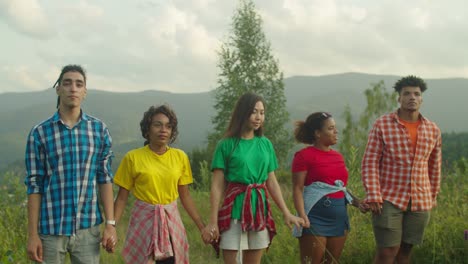 portrait of excited diverse multiracial travelers standing with arms raised on mountain peak