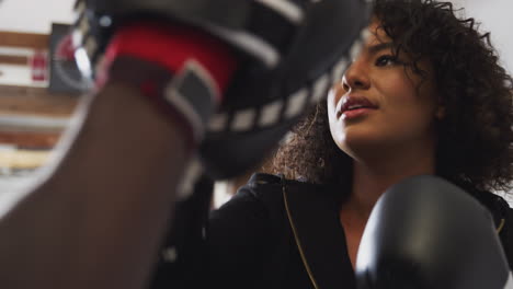 male boxing coach with female boxer in gym using training gloves