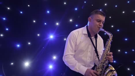tilt up shot of biracial jazz musician in checkered suit and bowtie playing saxophone while sitting against black band member in dimly lit bar, rehearsing and checking sound before live performance