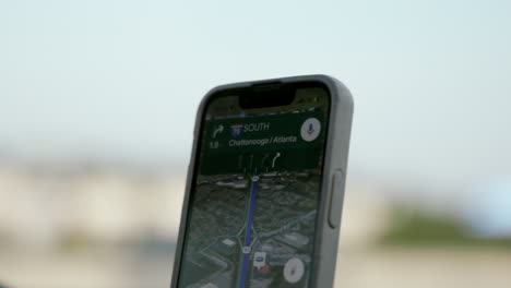 a smartphone gps screen displays a navigation route toward i-75 south with directions to chattanooga and atlanta, held up against a pale sky backdrop.