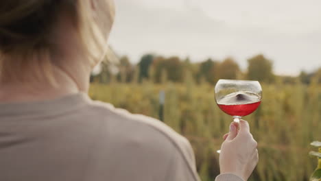 a woman with a glass of red wine stands near a vineyard. tasting and wine tour