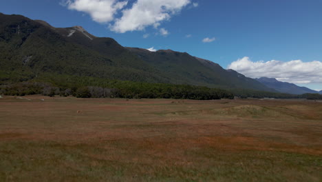 Aerial-view-of-a-car-driving-across-an-open-grassy-field-in-Fiordland-Southland,-New-Zealand