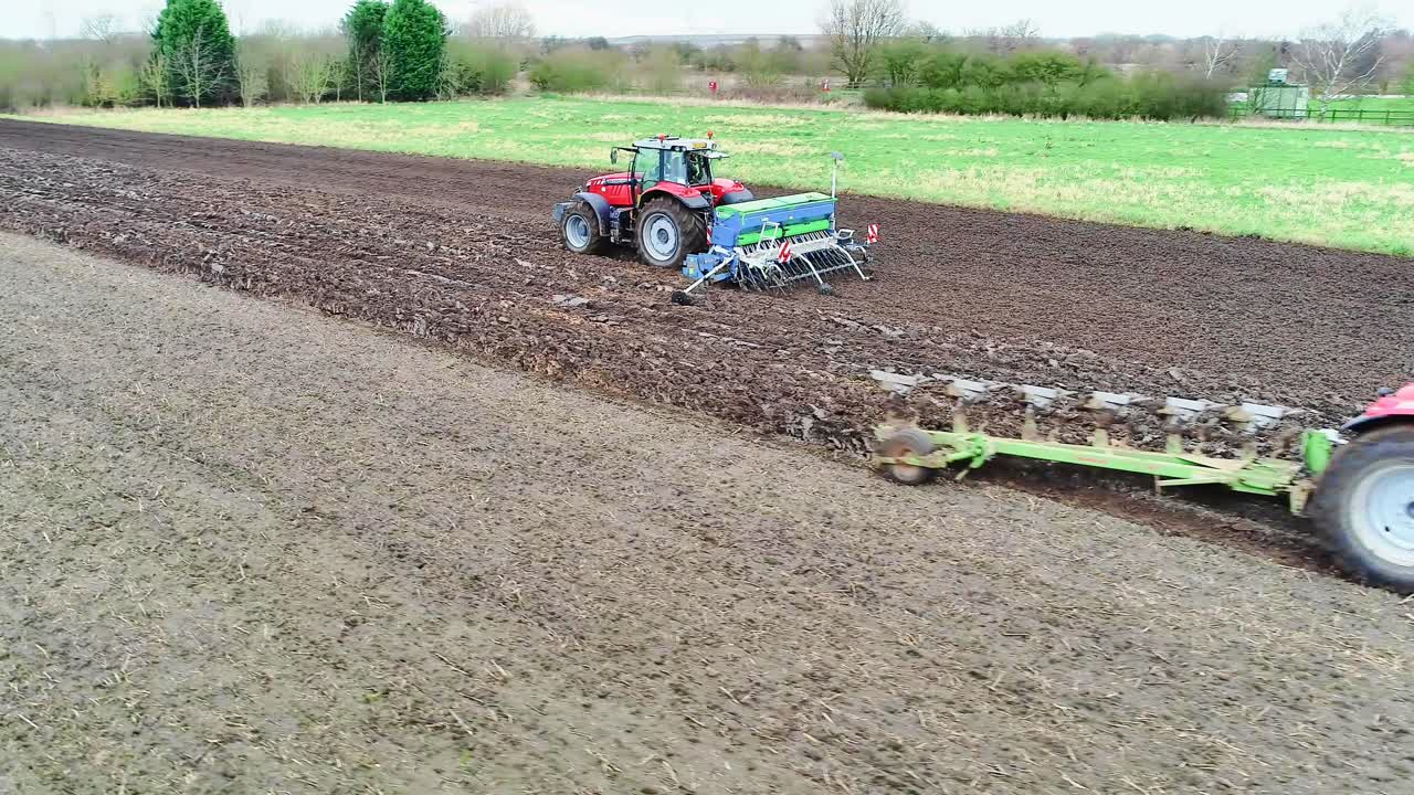 Aerial clip of a plough and seed drill crossing over in a field as the farmers work to get the next wheat crop drilled.