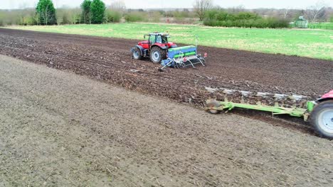 aerial clip of a plough and seed drill crossing over in a field as the farmers work to get the next wheat crop drilled.