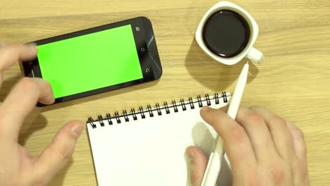 el especialista está sentado en el escritorio. en una mano el mango. la otra mano trabaja con la tableta. una taza de café en la mesa. pantalla verde.