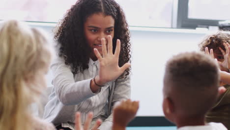 infant school children in class raising hands, learning to count with their female teacher, close up