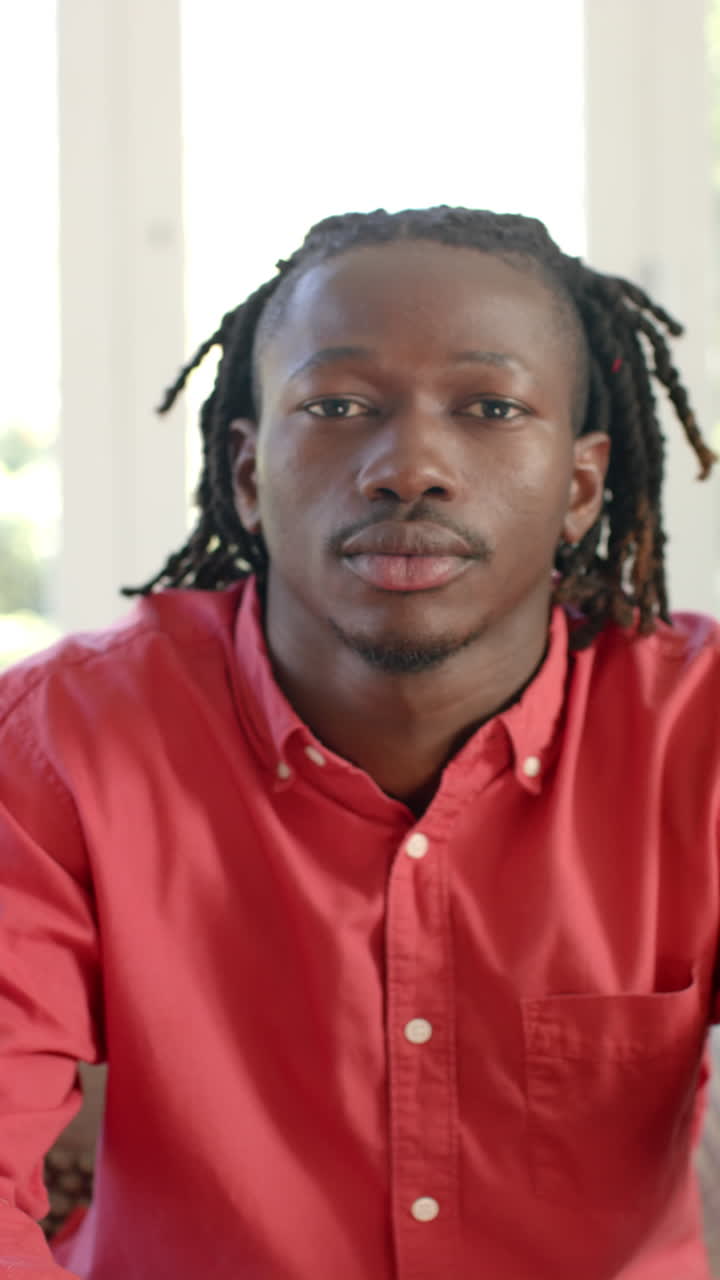 Vertical video portrait of african american man with dreadlocks smiling in sunny room, slow motion